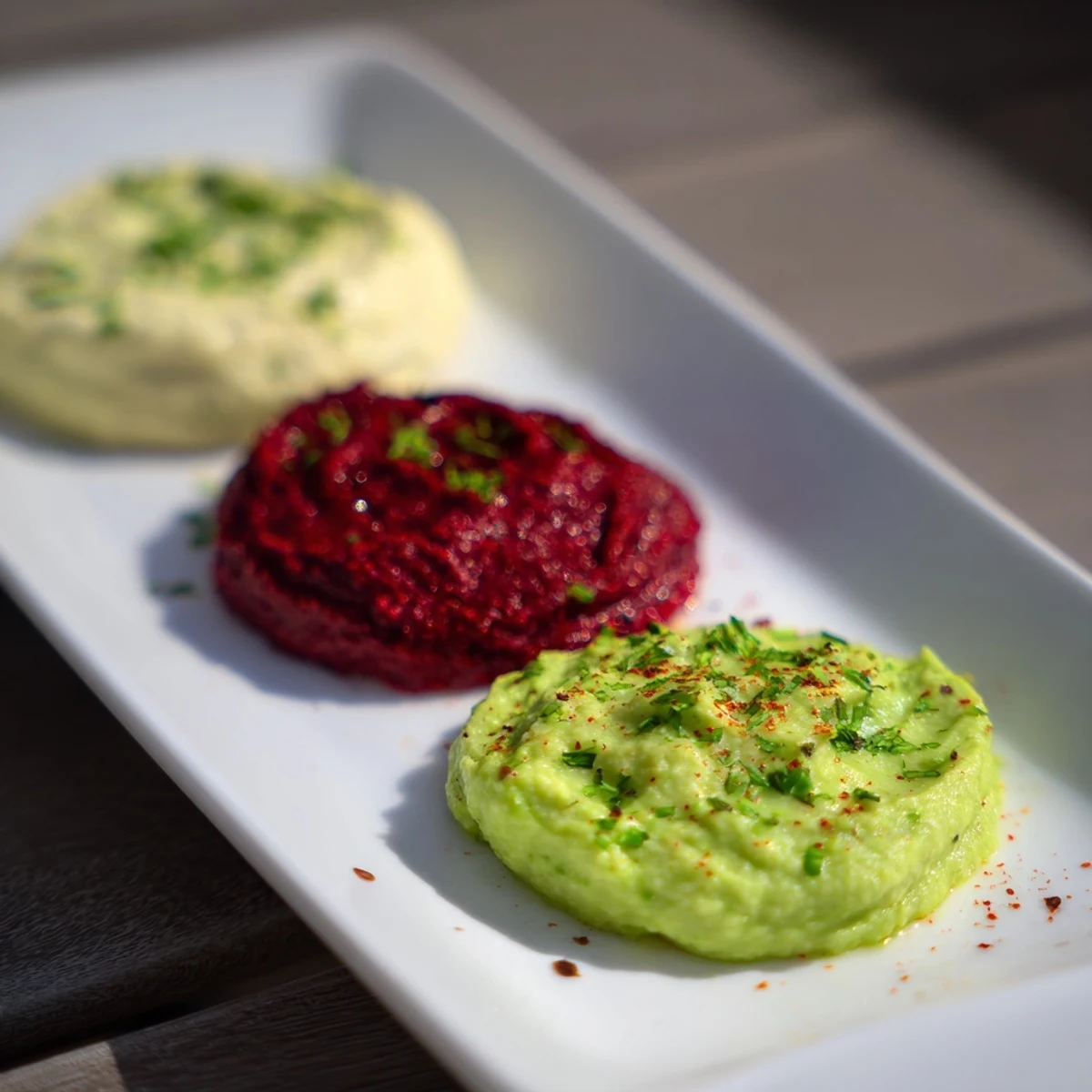 A colorful presentation of Dip Trio: three dips arranged side-by-side with fresh vegetables for dipping.