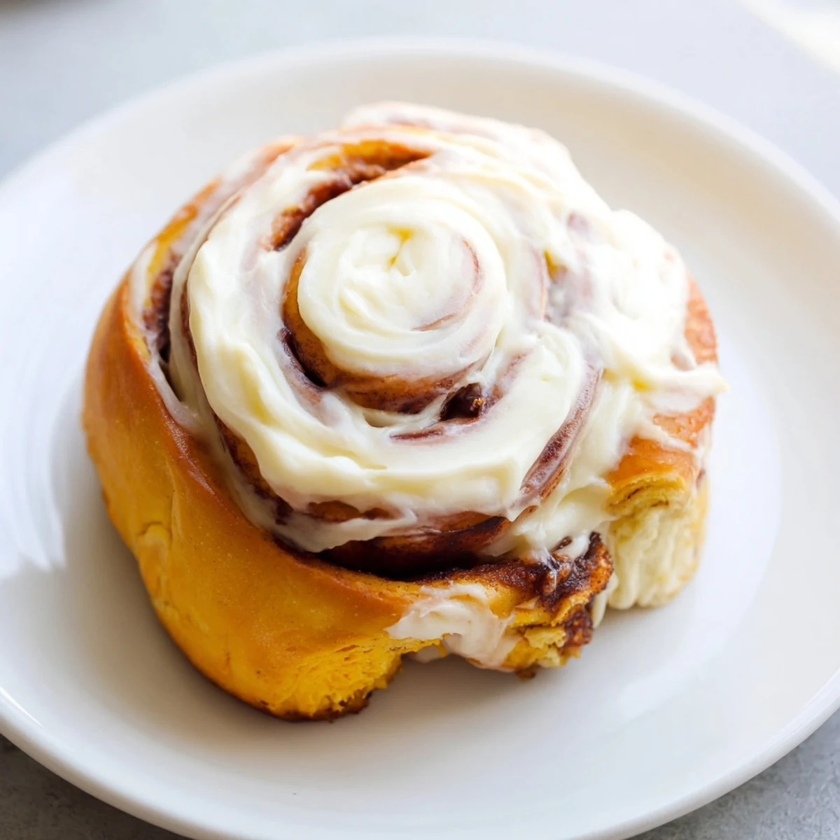 Freshly baked pumpkin cinnamon rolls with cream cheese frosting swirled on top, displayed on a rustic wooden board.