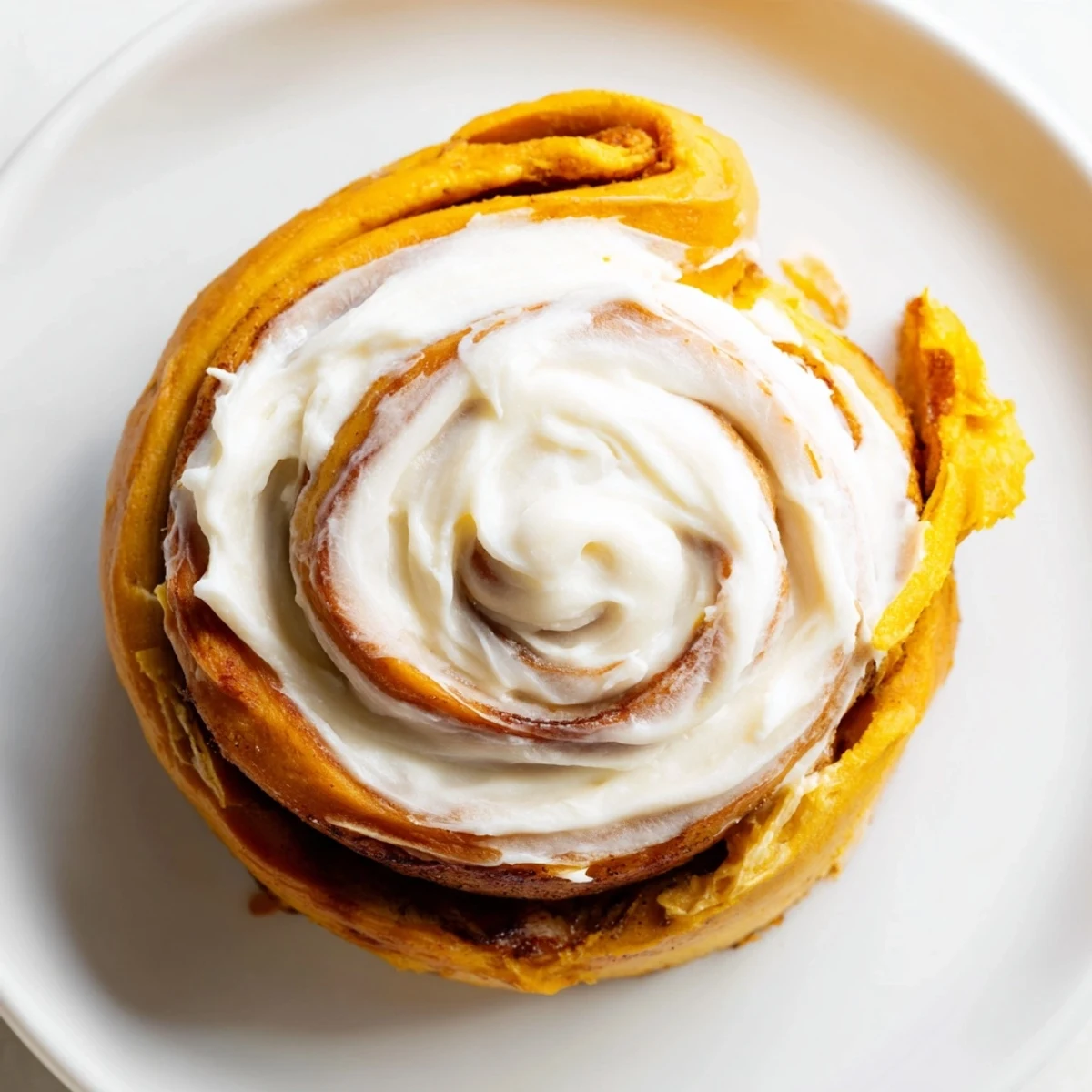 A close-up of pumpkin cinnamon rolls drizzled with cream cheese frosting, revealing gooey cinnamon sugar filling inside.