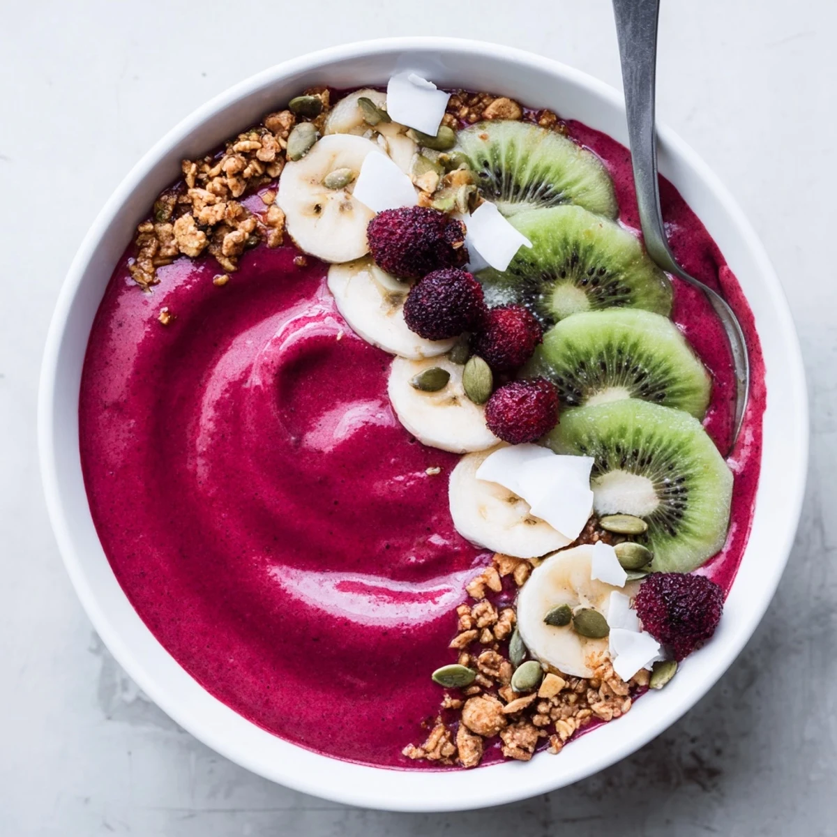 Two bowls of colorful Beet and Berry Smoothie Bowl, garnished with sliced kiwi, shredded coconut, and mint leaves.