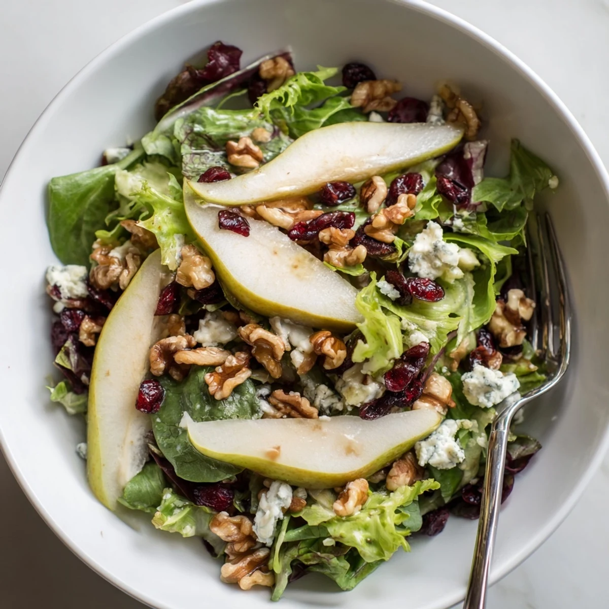 A colorful bowl of Pear Gorgonzola Salad features crumbled cheese, toasted walnuts, and glistening vinaigrette, ready to serve as a light meal.