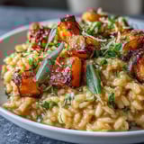 Two forks hovering over a bowl of Vegan Pumpkin Risotto, garnished with crispy sage leaves and a sprinkle of nutritional yeast.