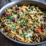 Savory Comforting Ground Beef Orzo Dinner served in a skillet, featuring sweet bell peppers and peas in a rich tomato broth.