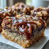 Freshly baked Decadent Sweet and Chewy Turtle Bars with Chocolate and Caramel cut into squares on a marble slab, drizzled with melted chocolate and sea salt.