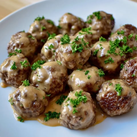 Steaming plate of Swedish Meatballs swimming in a creamy, savory sauce, ready for serving.