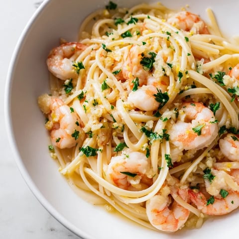 Bright garlic butter shrimp linguine glistening with lemon zest and fresh parsley, served hot in a white bowl.