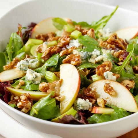 A close-up of Apple and Walnut Salad with sliced crisp apples, celery, and toasted walnuts on greens, drizzled with tangy vinaigrette.  