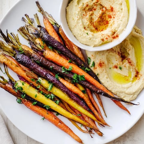Vibrant roasted rainbow carrots arranged on a platter with creamy, tahini-rich homemade hummus, garnished with parsley and paprika.  