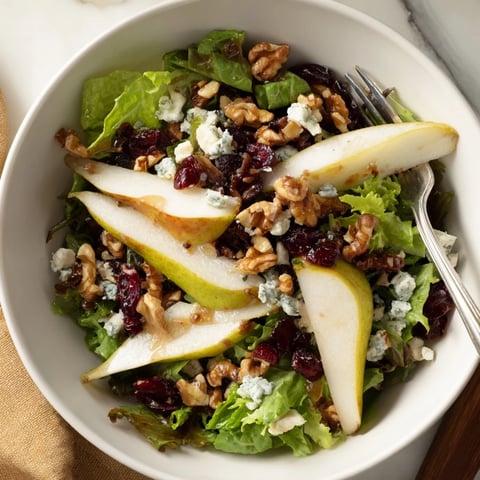 Freshly sliced pears and crumbled Gorgonzola top a bed of mixed greens, garnished with toasted walnuts for a perfect Pear Gorgonzola Salad.