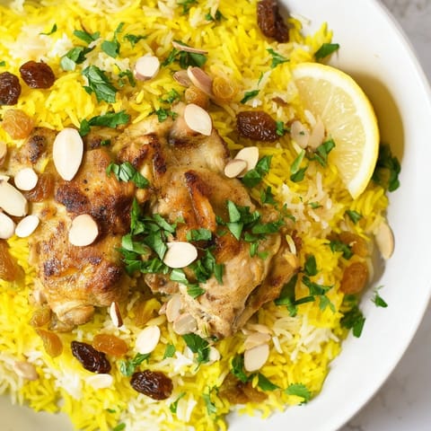 Steaming saffron chicken and rice pilaf, with visible herbs and toasted almonds on top.