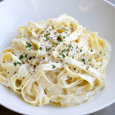 A steaming bowl of Pasta Alfredo Cottage Hack, showing off the perfectly coated fettuccine pasta.