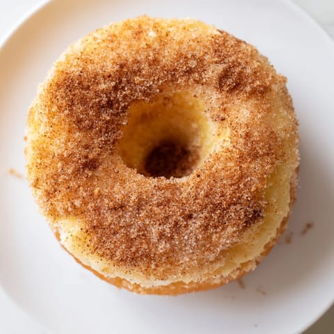 Fluffy biscuit dough donuts coated in sparkling cinnamon sugar, stacked on a rustic wooden board.
