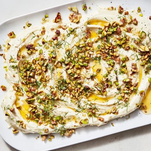 Soft, creamy butter forms the base of this Flavored Butter Board Charcuterie, garnished with pistachios and dill, served alongside sliced baguette and crackers on a rustic platter.