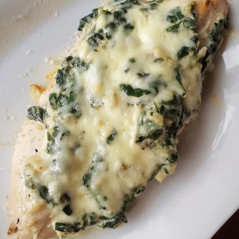 A close-up of the Spinach & Artichoke Chicken Bake with melted cheese and wilted greens.