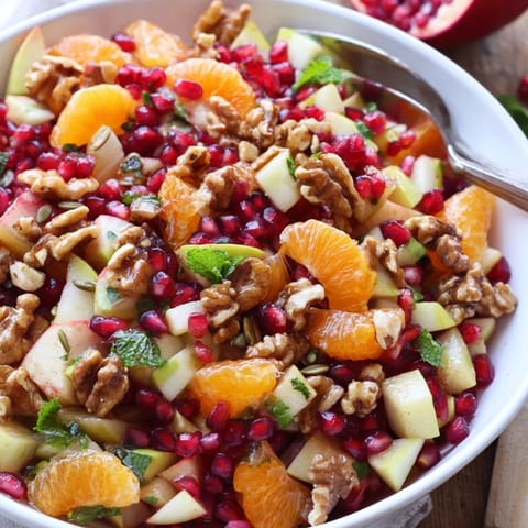 A serving of Pomegranate and Walnut Salad in a white bowl, featuring fresh mint and a light honey-lemon dressing drizzle.