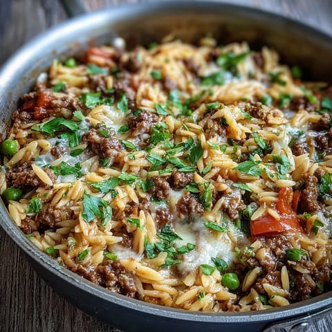 Savory Comforting Ground Beef Orzo Dinner served in a skillet, featuring sweet bell peppers and peas in a rich tomato broth.
