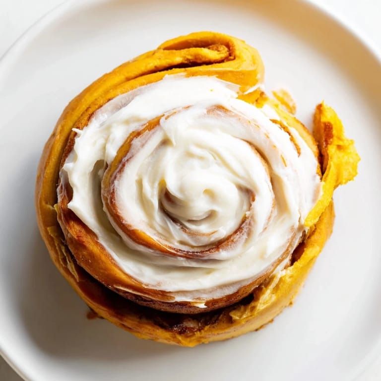 A close-up of pumpkin cinnamon rolls drizzled with cream cheese frosting, revealing gooey cinnamon sugar filling inside.