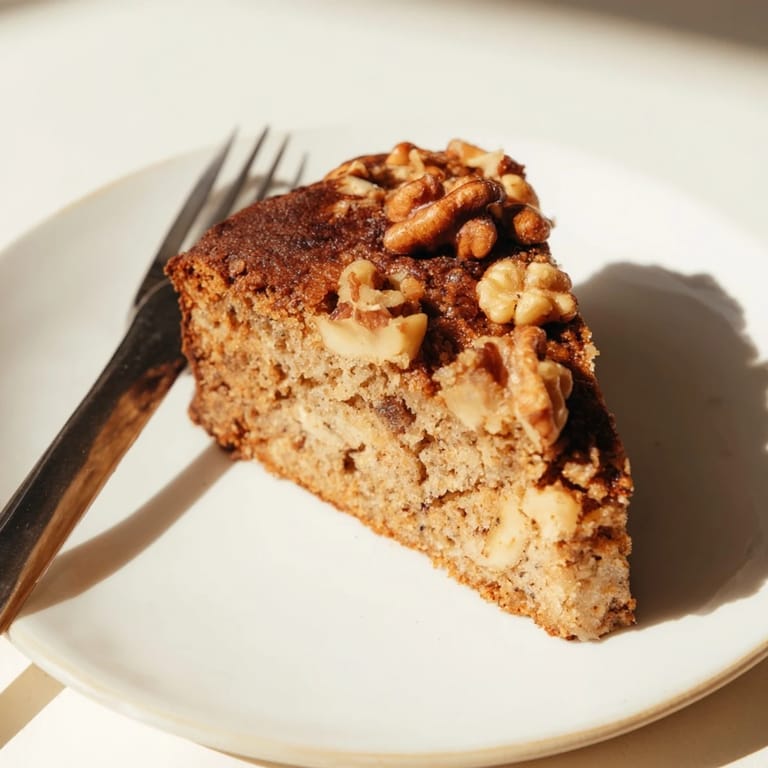 Golden-brown banana bread loaf with chopped walnuts, sliced thick and ready for breakfast with a cup of coffee.  